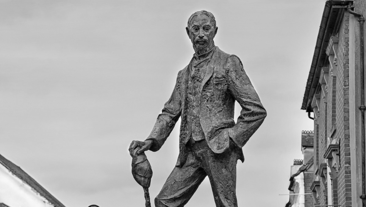 Bronze statue of man with cane and hat.