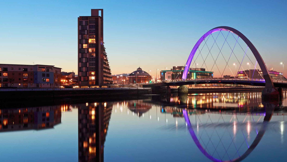 Modern bridge over river at twilight, illuminated buildings.